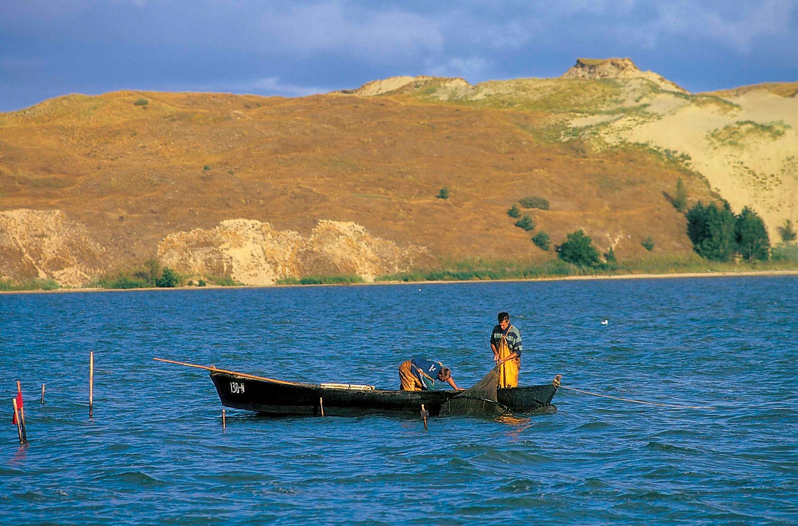 Fishers in a boat on the Curonian Lagoon in front of the dunes